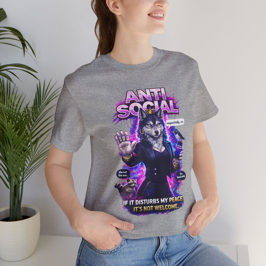A smiling woman wears the Anti Social She-Wolf T-Shirt — Funny Introvert Graphic Tee, featuring a gray design with a colorful cat in a suit and the text "ANTI-SOCIAL" and "If it disturbs my peace, it's not welcome," standing indoors by a plant.