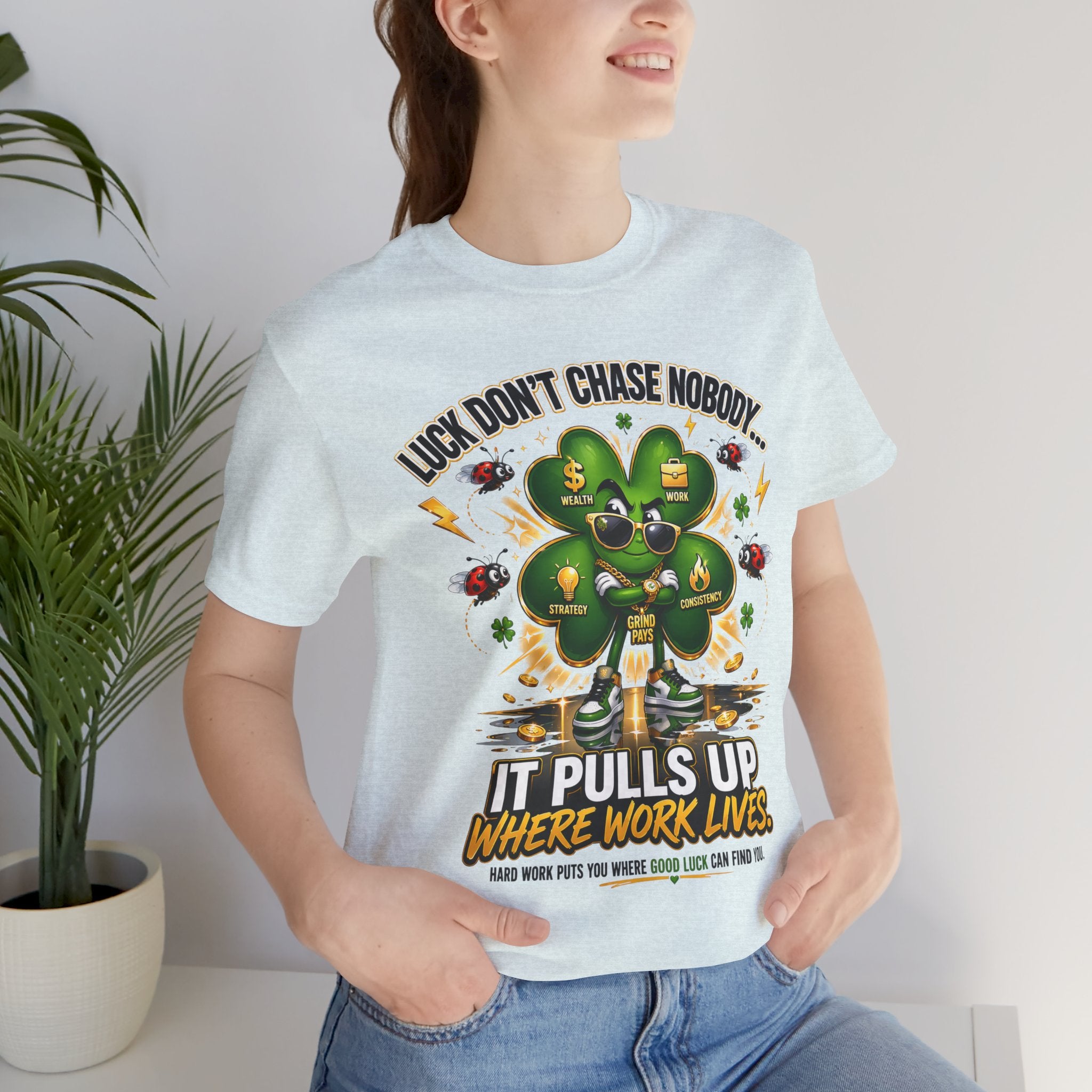 A woman smiles by a potted plant, wearing the TimeWarp Drip Lucky Clover "Pulls Up Lives" Graphic T-Shirt (sizes S-3XL), featuring a cartoon clover with sunglasses and cash. The shirt reads: Luck Don’t Chase Nobody... It Pulls Up Where Work Lives.