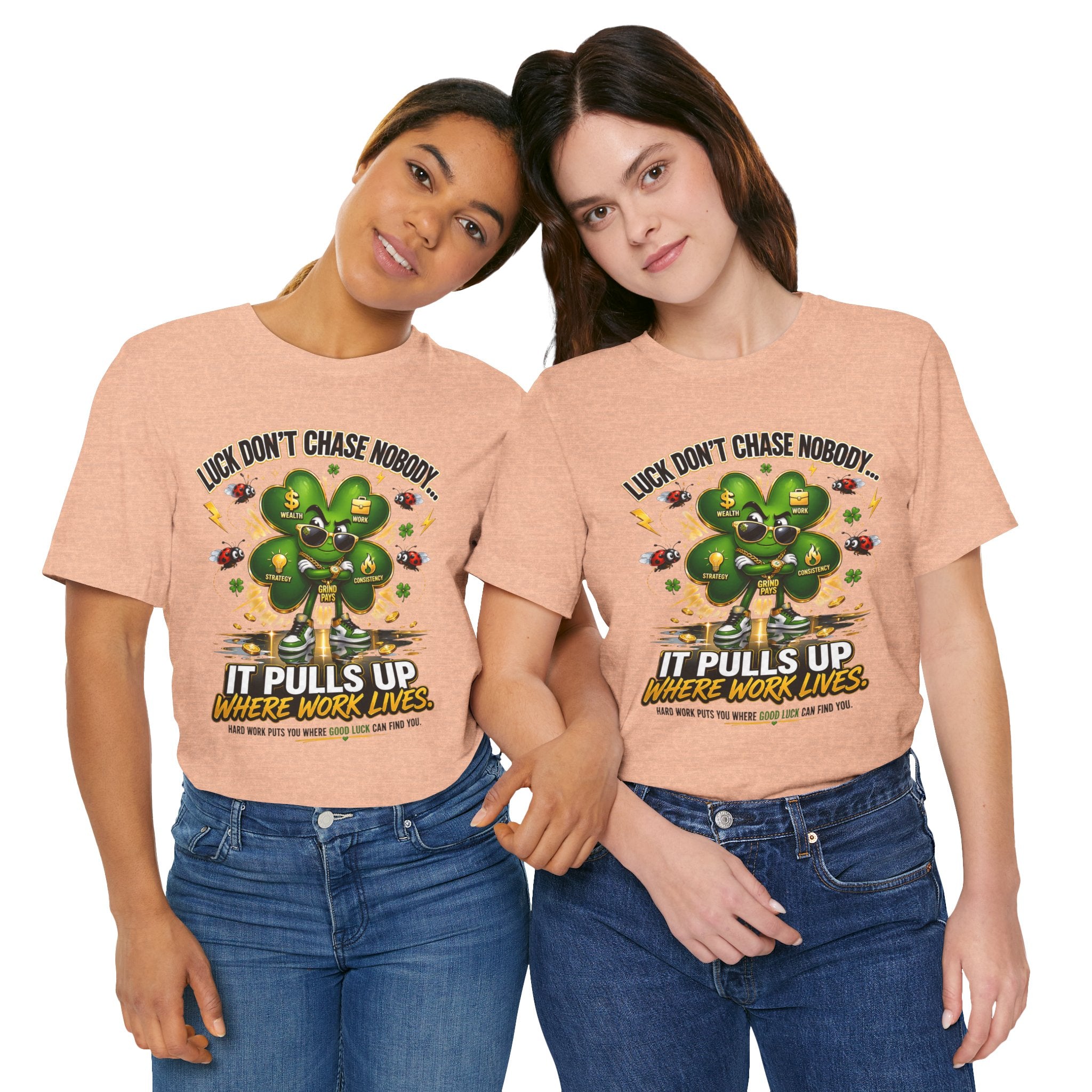Two women pose together wearing TimeWarp Drip's Lucky Clover "Pulls Up Lives" Graphic T-Shirt in peach (sizes S-3XL), featuring a four-leaf clover and the phrase: Luck don’t chase nobody. It pulls up where work lives. Both smile casually.