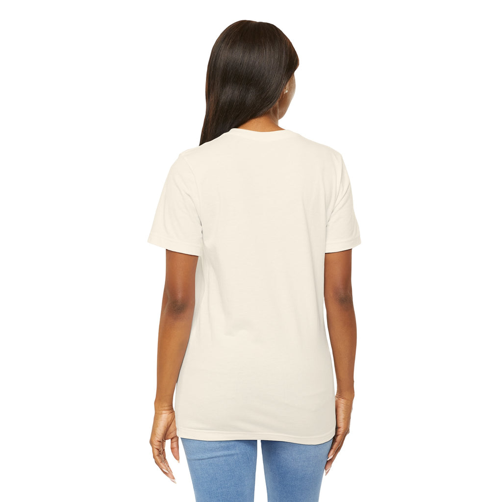 A woman with long dark hair stands with her back to the camera, wearing a TimeWarp Drip Lucky Clover "Pulls Up Lives" graphic T-shirt (S-3XL) and light blue jeans against a white background.