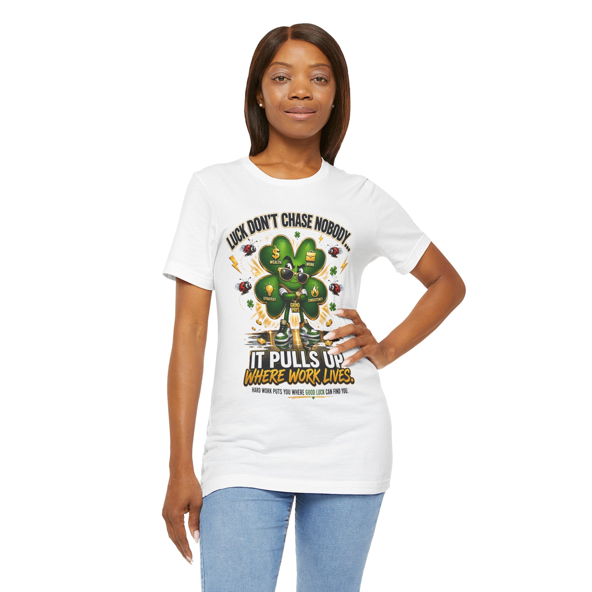 A woman with straight brown hair smiles in a TimeWarp Drip Lucky Clover "Pulls Up Lives" Graphic T-Shirt (sizes S-3XL), featuring a lucky clover, gold coins, and the phrase: “Luck don’t chase nobody, it pulls up where work lives.”.