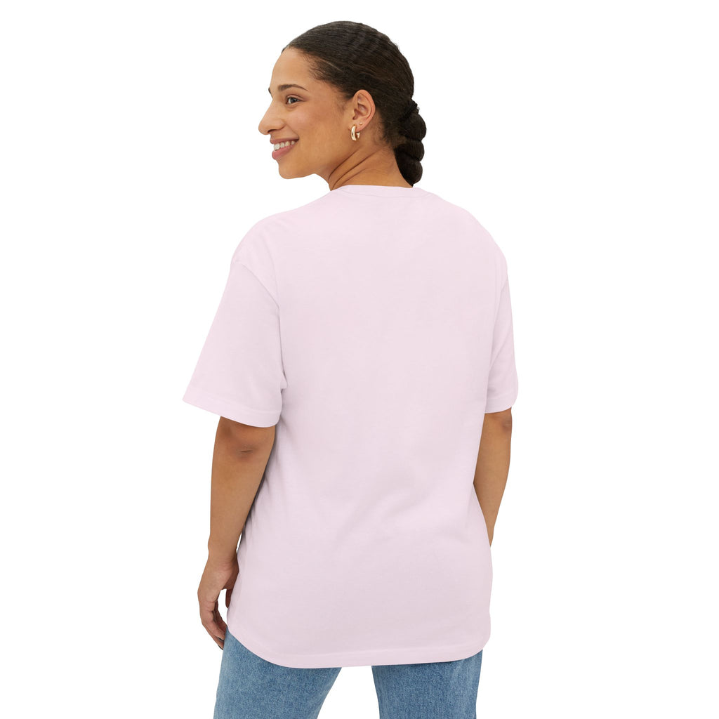 A woman with braided hair smiles over her shoulder, wearing the Crowned In Every Era Unisex Oversized Boxy Tee in light pink and blue jeans, standing against a white background.
