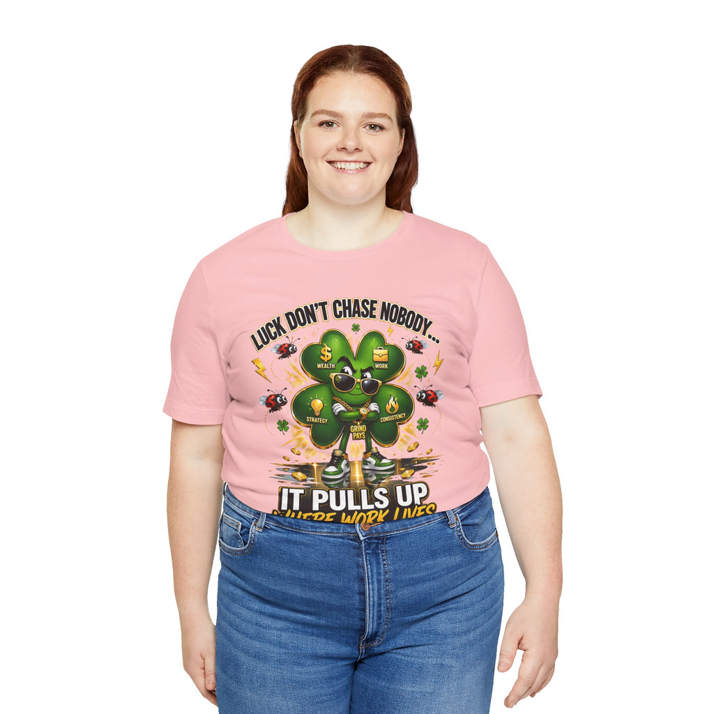 A smiling woman with long brown hair models a pink size S "Lucky Clover, 'Pulls Up Lives'" graphic T-shirt by TimeWarp Drip, adorned with a four-leaf clover, bees, and the phrase: Luck doesn’t chase nobody. It pulls up where work is. She stands before a white background.