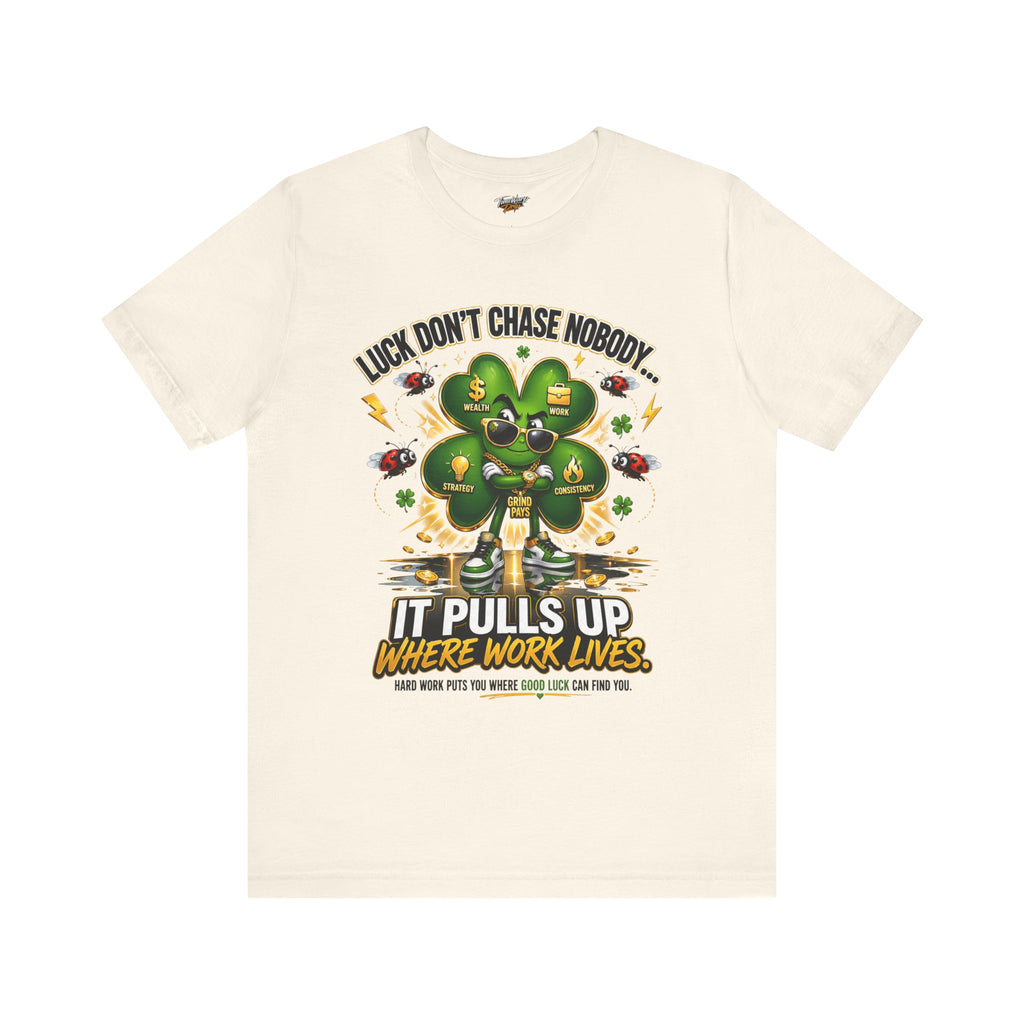 The Lucky Clover "Pulls Up Lives" Graphic T-Shirt comes in cream and sizes S–3XL, featuring a large green four-leaf clover with icons, words like “Work,” and the text: “Luck don’t chase nobody. It pulls up where work lives.”.