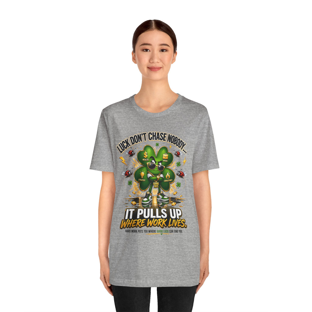 A smiling woman wears the TimeWarp Drip Lucky Clover "Pulls Up Lives" Graphic T-Shirt, available in gray sizes S-3XL, featuring a cartoon four-leaf clover lifting weights and the phrase: Luck don’t chase nobody—it pulls up where work lives.