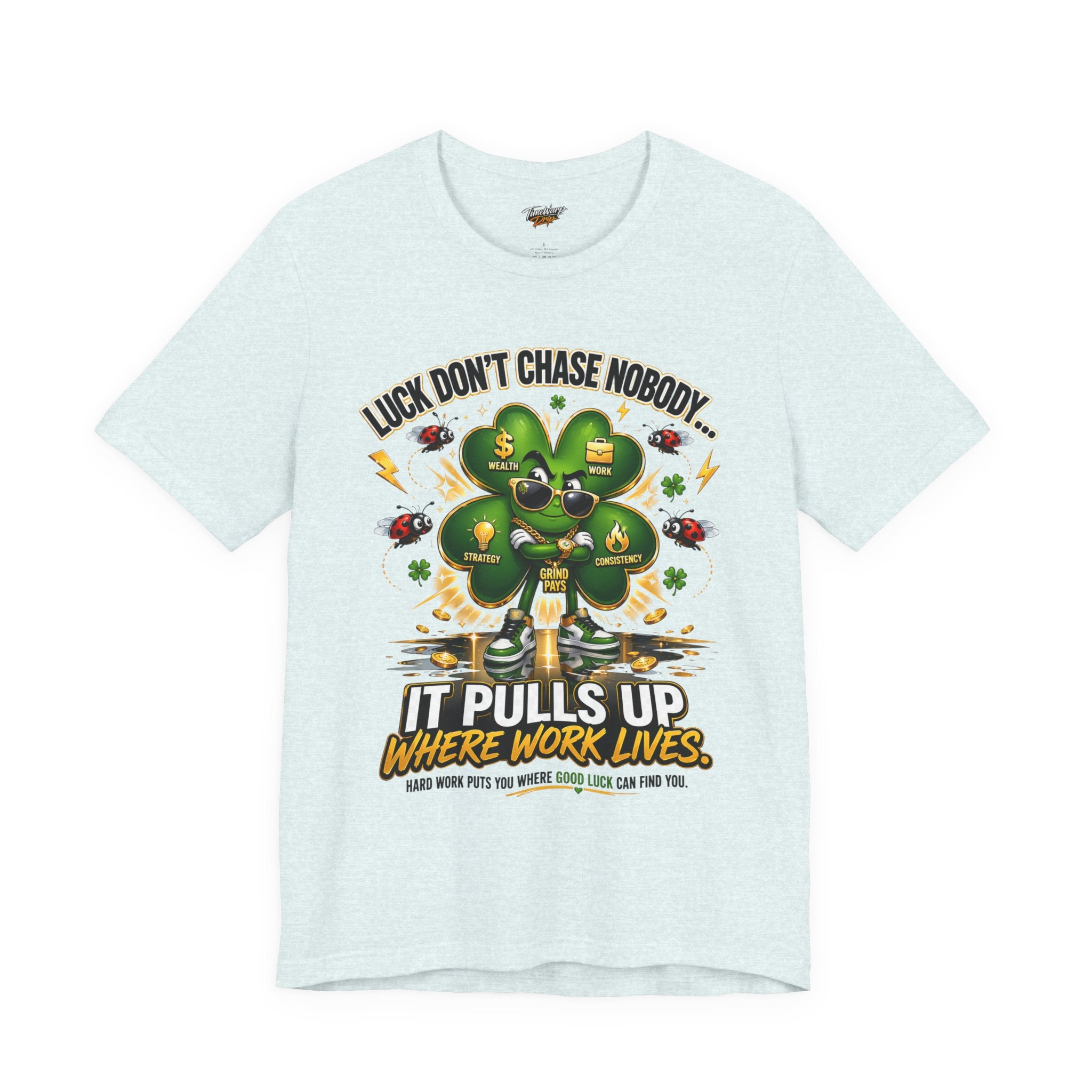 The Lucky Clover "Pulls Up Lives" Graphic T-Shirt comes in light colors and S–XL plus sizes. It displays a cartoon clover with sunglasses and gold shoes amid lucky symbols, reading: “Luck doesn’t chase nobody… it pulls up where work lives.”.