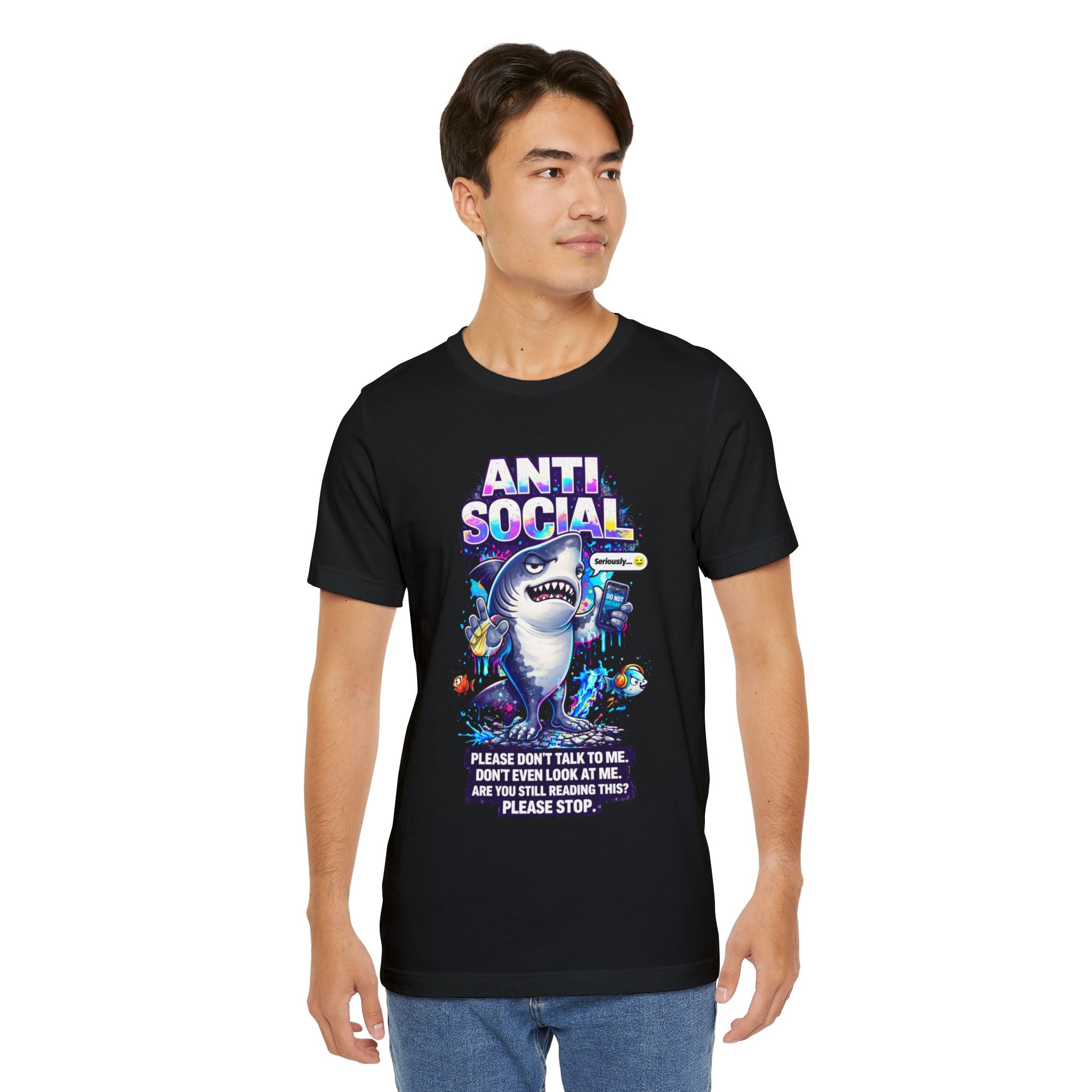 A young man wears the Anti Social Shark T-Shirt — Funny Introvert Graphic Tee, a unisex cotton shirt with a colorful cartoon shark and phrases like "ANTI-SOCIAL" and "Please don’t talk to me. Are you still reading this? Please stop.